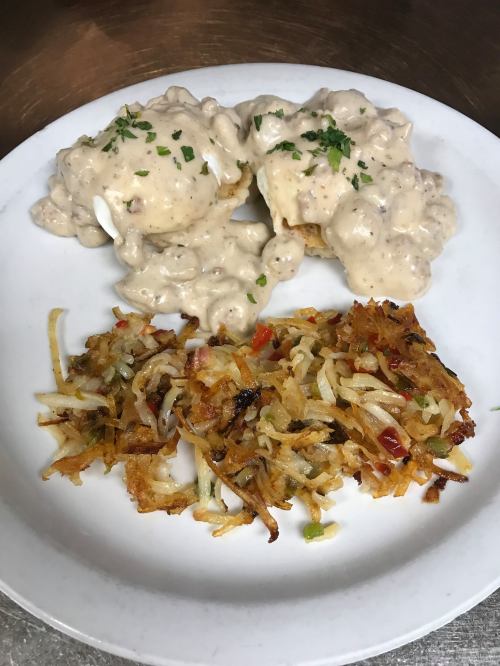 Plate of biscuits smothered in creamy gravy, served with crispy hash browns on the side, garnished with parsley.