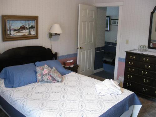 Cozy bedroom with a bed, decorative pillows, a dresser, and a door leading to another room. Wall art adds charm.