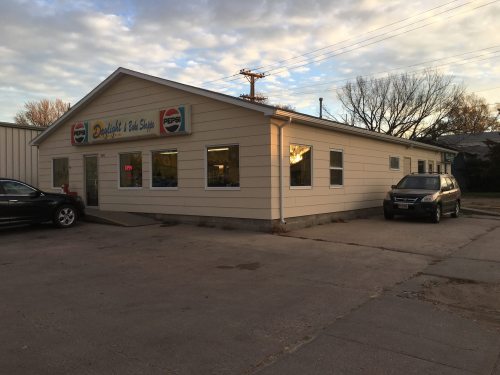 A single-story building with a sign for a barbershop, featuring large windows and a parked car in front.