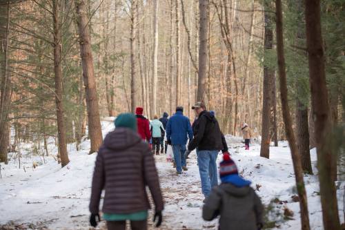 A group of people walking on a snowy forest trail, surrounded by trees in winter.