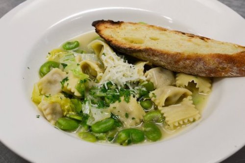 A bowl of pasta with green fava beans, herbs, and a slice of toasted bread on the side.