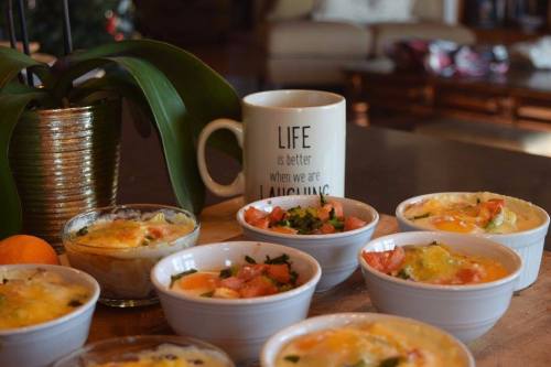 A cozy kitchen scene featuring bowls of baked eggs, a mug with a motivational quote, and a potted plant.