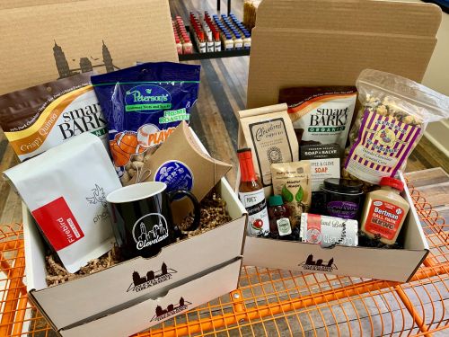 Two gift boxes filled with snacks, coffee, soap, and a mug, arranged on an orange shopping cart.