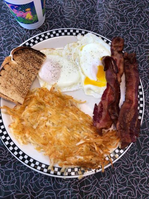 A plate of breakfast featuring two eggs, crispy bacon, hash browns, and toasted bread.