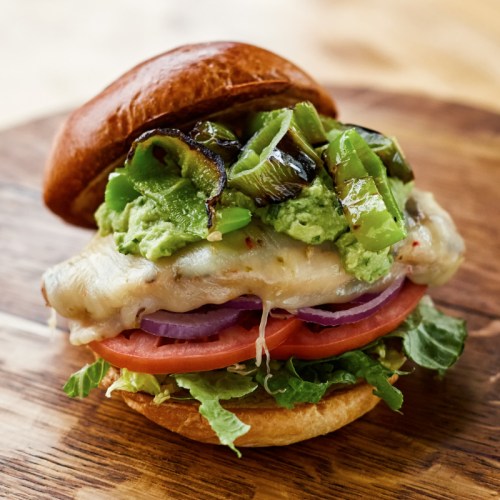 A delicious sandwich with grilled peppers, melted cheese, lettuce, tomato, and guacamole on a toasted bun.