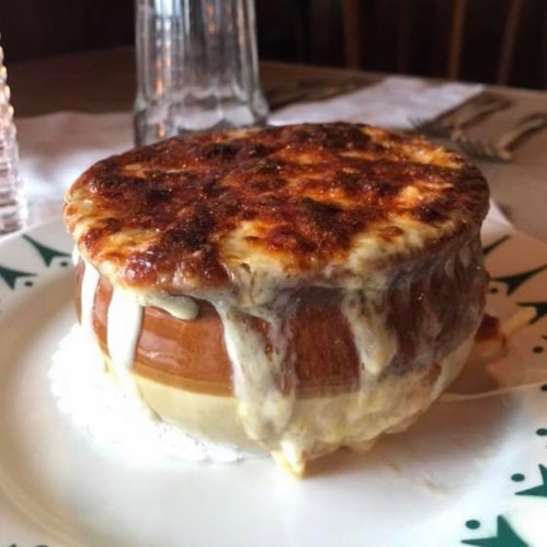 A bubbling bowl of French onion soup topped with melted cheese, served on a decorative plate.