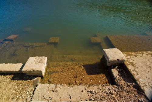 A view of submerged stone steps leading into calm water, with a sandy bottom visible beneath the surface.