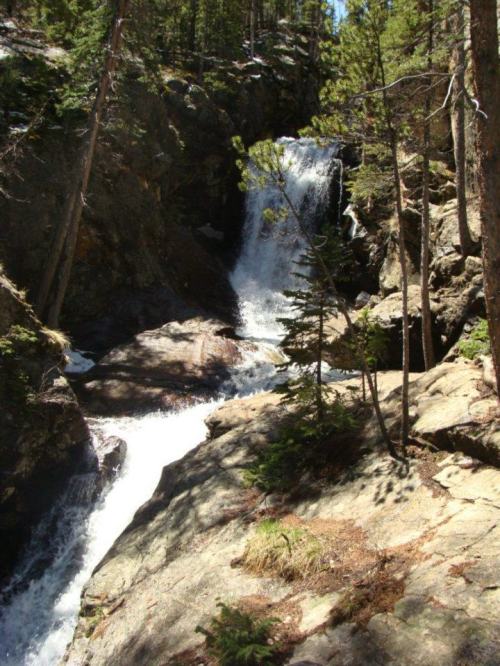 A serene waterfall cascading over rocky terrain, surrounded by lush green trees and natural scenery.