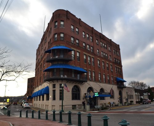 Historic brick building with blue awnings, located at a street corner, featuring American flags and a cloudy sky.