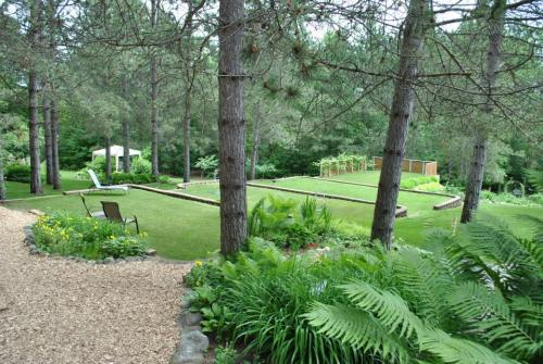 Lush garden with green grass, trees, and a stone path, featuring a seating area and raised garden beds.