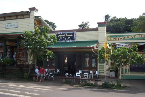 A quaint ice cream shop with outdoor seating, surrounded by tropical greenery and colorful storefronts.