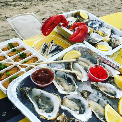 A seafood feast featuring oysters on ice, a red lobster, and crab cakes with lemon wedges and dipping sauces.