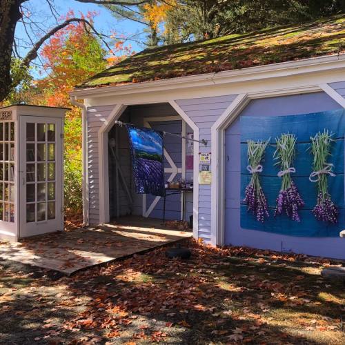 A quaint garage with purple flower displays and a vintage phone booth, surrounded by autumn leaves.