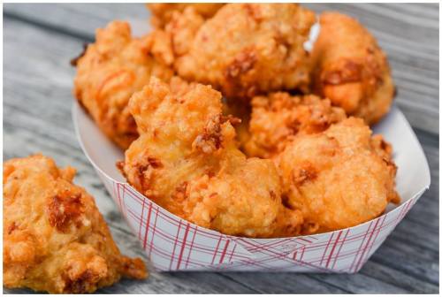A close-up of golden-brown, crispy fried chicken pieces in a paper tray on a wooden surface.