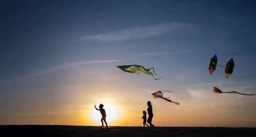 Silhouettes of children flying kites against a sunset sky, with colorful kites soaring above.