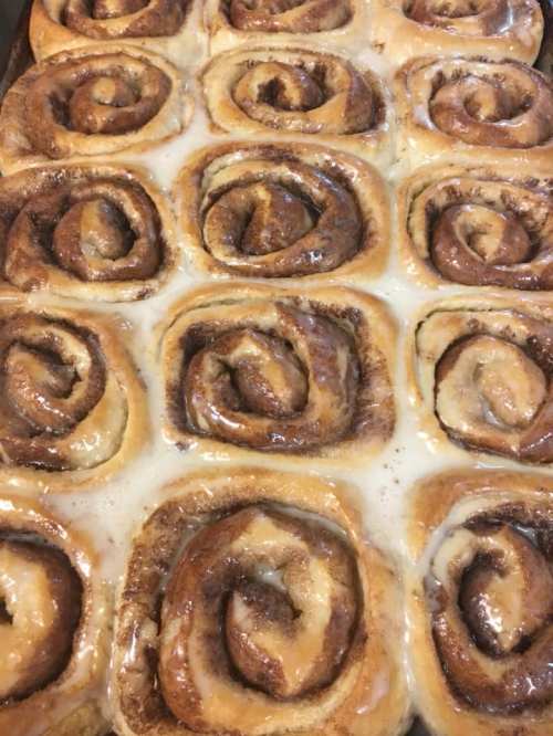 A close-up of freshly baked cinnamon rolls drizzled with creamy icing, arranged in a baking dish.
