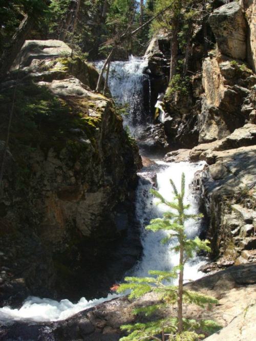 A serene waterfall cascading between rocky cliffs, surrounded by lush green trees in a natural setting.