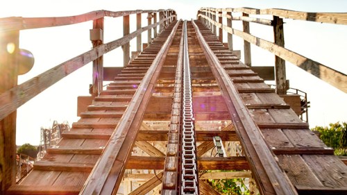 A wooden roller coaster track ascending into the sky, with sunlight shining through the structure.
