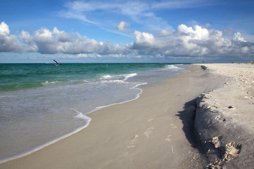 A serene beach scene with gentle waves, soft sand, and a blue sky dotted with clouds.