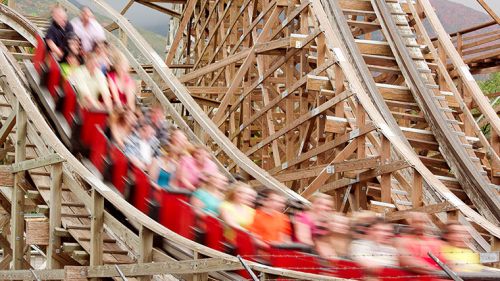 A blurred image of a wooden roller coaster with excited riders in red seats, capturing the thrill of the ride.