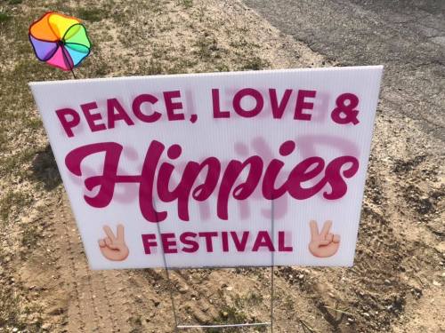 Sign for a "Peace, Love & Hippies Festival" with colorful graphics and peace symbols.