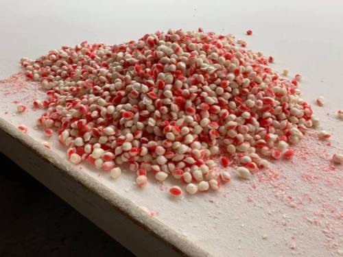 A mound of small, round candies with red and white stripes scattered on a white surface.