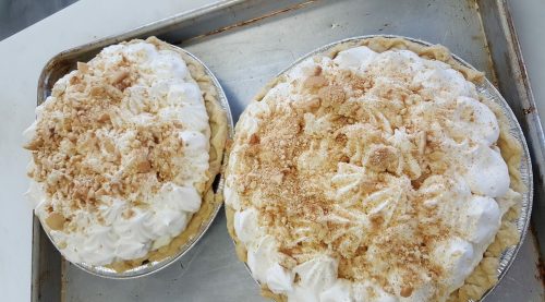 Two pies on a baking tray, topped with whipped cream and crushed cookies, showcasing a delicious dessert presentation.