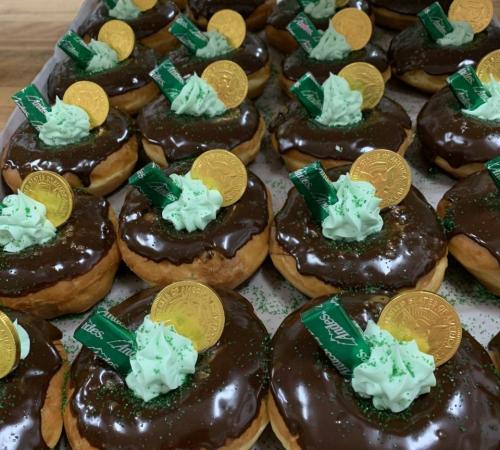A tray of chocolate-glazed donuts topped with green frosting, gold coins, and green sprinkles.