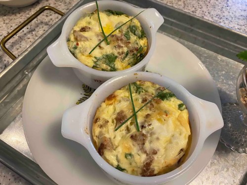 Two small white ramekins filled with baked egg dishes, topped with green herbs, on a decorative plate.