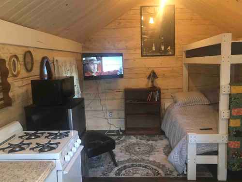 Cozy cabin interior with a bunk bed, kitchenette, TV, and rustic decor. Warm lighting enhances the inviting atmosphere.