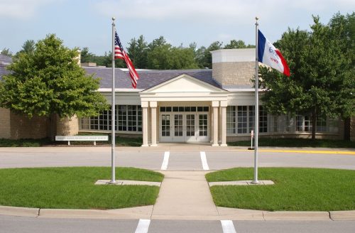 Front view of a building with American and Iowa flags, surrounded by green grass and trees.