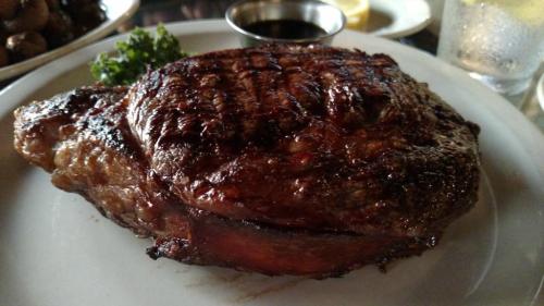 A perfectly grilled steak on a white plate, garnished with parsley and accompanied by a small bowl of sauce.
