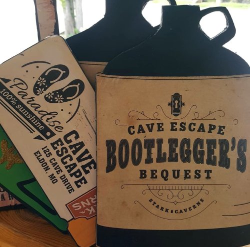 Signage for Cave Escape and Bootlegger's Bequest, featuring playful designs and location details in Eldon, MO.
