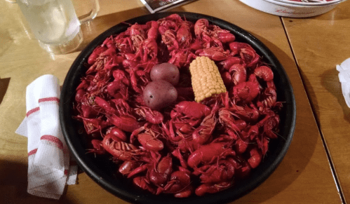 A large platter filled with red crawfish, potatoes, and corn, served on a wooden table.