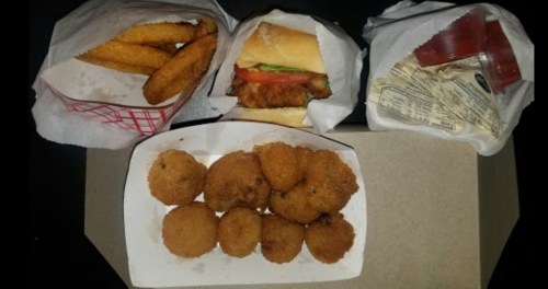 A variety of fast food items including fried snacks, a sandwich, and dipping sauces in takeout containers.