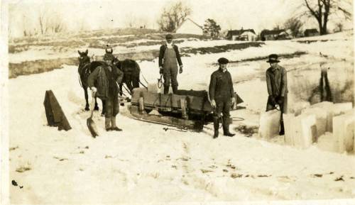 Men and horses working in the snow, with ice blocks and a sled in a rural landscape.