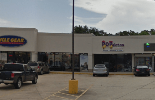A storefront with "Pop Paletas" sign next to "Cycle Gear," featuring parked cars and a cloudy sky.