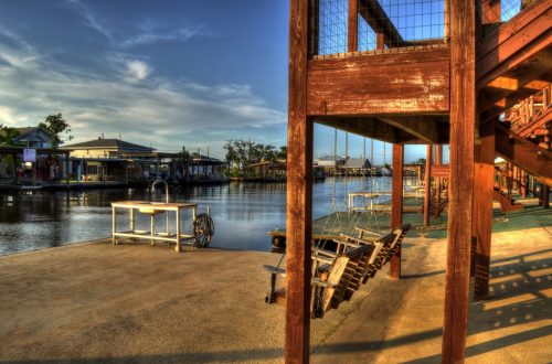 A serene waterfront scene featuring wooden structures, a dock, and calm water under a clear blue sky.