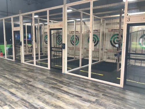 Indoor axe-throwing range with multiple lanes, wooden barriers, and target boards in a spacious setting.