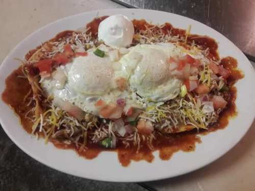 A plate of enchiladas topped with two poached eggs, cheese, diced tomatoes, onions, and a red sauce.