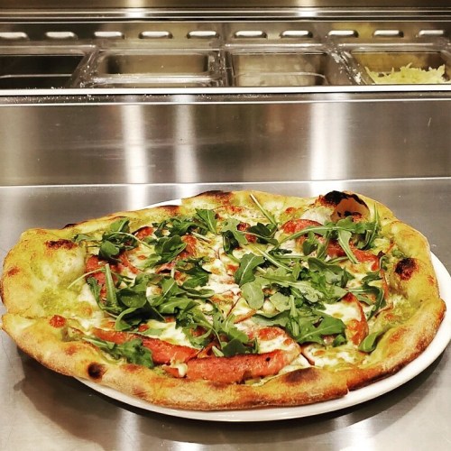 A freshly baked pizza topped with tomato sauce, mozzarella, and fresh arugula on a white plate.
