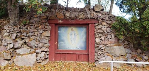 A stone wall with a wooden frame featuring a religious painting of a figure surrounded by clouds and doves.