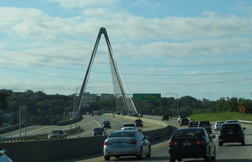 A view of a cable-stayed bridge with cars on a highway under a blue sky with scattered clouds.