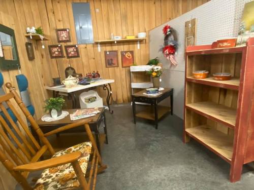 A cozy vintage room with wooden walls, featuring a rocking chair, shelves, and decorative items.