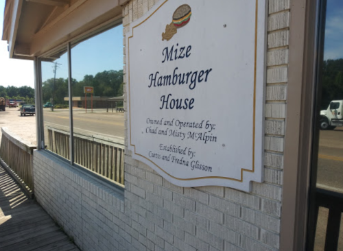 Sign for Mize Hamburger House, featuring owners' names and establishment details, mounted on a brick wall.