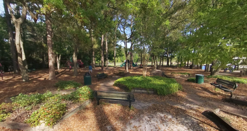 A serene park scene with benches, trees, and playground equipment surrounded by fallen leaves and greenery.