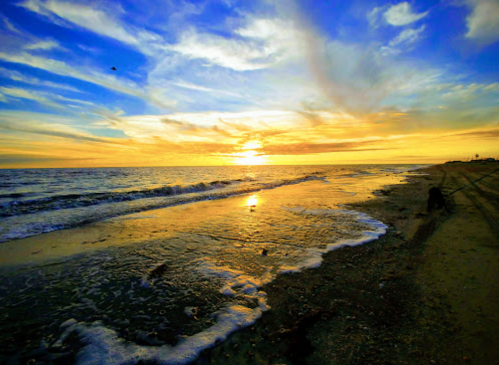 A vibrant sunset over the ocean, with waves gently lapping at a sandy beach under a colorful sky.