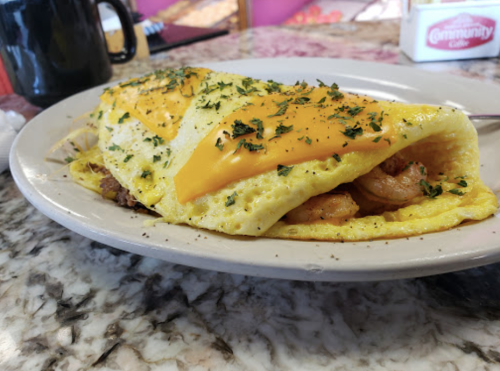 A fluffy omelet filled with shrimp and topped with melted cheddar cheese, garnished with herbs on a plate.