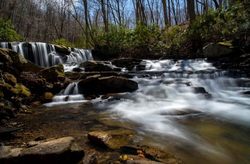 A serene waterfall cascades over rocks, surrounded by trees and greenery in a tranquil forest setting.