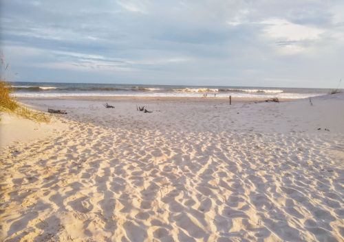 A serene beach scene with soft sand, gentle waves, and a cloudy sky in the background.